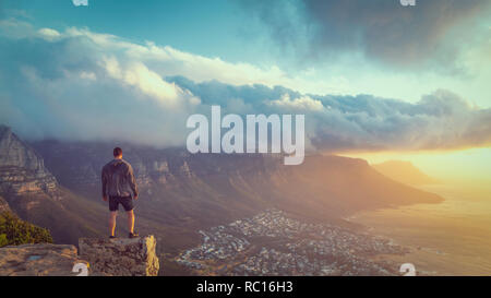 Young man standing on the edge at the top of Lion's head mountain in Cape Town with a beautiful sunset view Stock Photo