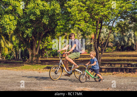 Happy family is riding bikes outdoors and smiling. Father on a bike and son on a balancebike Stock Photo