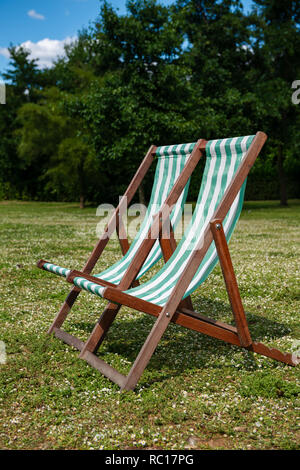 Striped deck chairs on the english lawn with forest trees on the background Stock Photo
