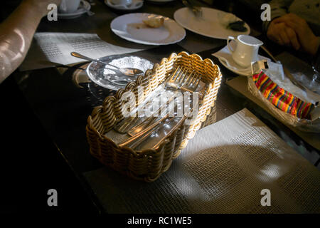 People eating at the messy table, a wicker basket with silverware in the center of image, indoor contrast shot Stock Photo