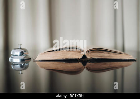 Opened old book and bell with reflected in brown surface. Hotel time Stock Photo