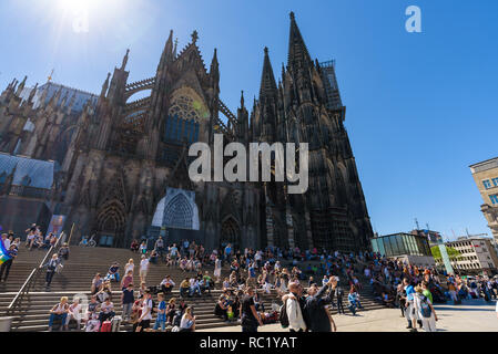 Cologne, Germany - May 2018. Local people and tourists sitting on the steps of the Cathedral and walking in the square in front of the Central Station Stock Photo