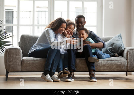 Happy african family with 2 children having fun with gadget  Stock Photo