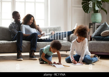 African parents relaxing on sofa while kids playing together dra Stock Photo