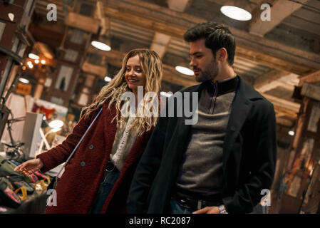 Stroll through the market together. Happy young joyful couple choosing handmade stuff and walking in rows at small street market. Autumn season, blond Stock Photo