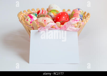 Colorful Easter eggs in wooden basket with piece of paper with space for text isolated on white background. Easter holiday concept. Stock Photo