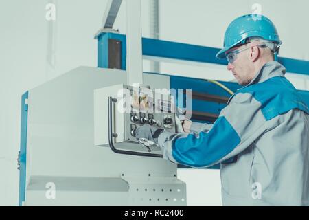 Factory Technician Worker. Caucasian Men Wearing Hard Hat and Safety Glasses Operating Heavy Duty Metal Cutter. Stock Photo