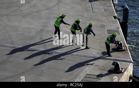 Four port workers pulling a mooring rope ashore in Lisbon  Four port workers are starting to pull ashore the mooring ropes of a cruise ship Stock Photo