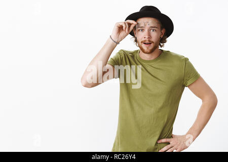 Look what we have here. Portrait of intrigued and interested cute charismatic boyfriend with beard in hat taking off glasses as seeing curious thing looking at camera surprised over gray background Stock Photo