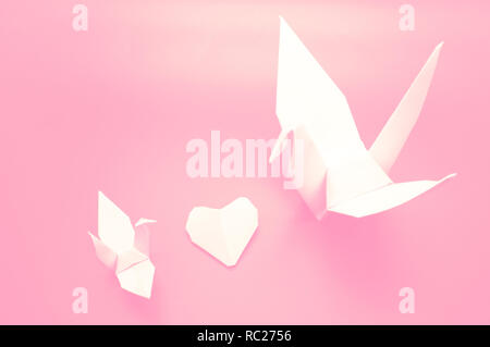 White origami crane and heart between, bird paper on pink background , Concept Valentine day Stock Photo