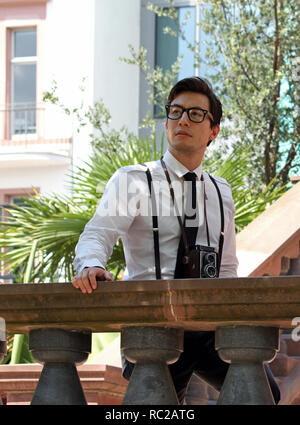 Young man wearing suspenders and glasses looking out from a large terrace Stock Photo
