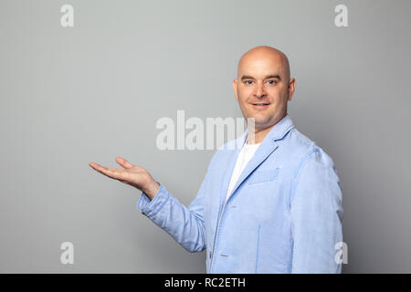 Cute bald man in a jacket and t-shirt shows against a gray wall Stock Photo