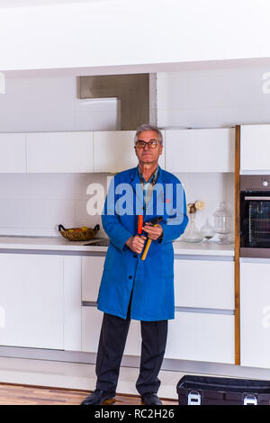 Mature worker standing near toolbox in the kitchen while holding hammer in hs hands Stock Photo