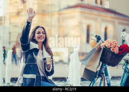 https://l450v.alamy.com/450v/rc2j19/beautiful-young-smiling-woman-with-bicycle-holding-cup-of-coffee-and-waving-hand-on-city-street-beauty-fashion-and-lifestyle-rc2j19.jpg