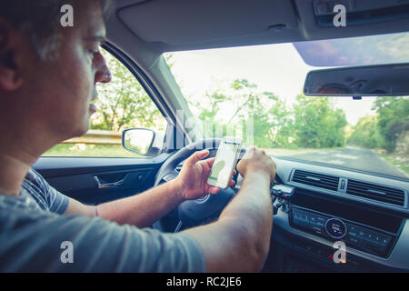 Young reckless man using his smartphone behind the wheel Stock Photo