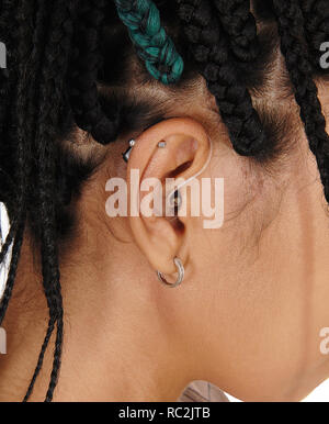 A woman wearing a modern hearing aid behind her ear in a close up image and braided black hair Stock Photo