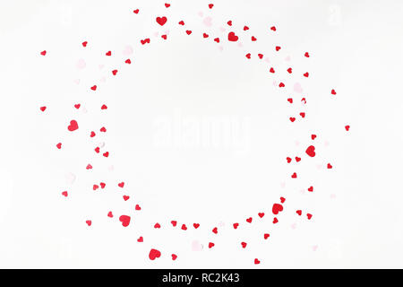 Valentines day or wedding festive composition. Circle made of red and pink paper heart shaped confetti isolated on white table background. Party decoration, celebration concept. Flat lay, top view. Stock Photo