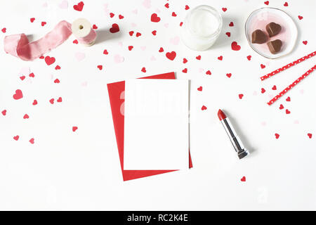 Valentines day, wedding still life scene. Candle, paper confetti, chocolate hearts, lipstick and blank greeting card mockup on white table background. Love concept. Flat lay, top view. Stock Photo