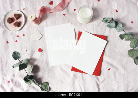 Valentines day, wedding stationery mockup scene. Candle, hearts confetti, chocolate, eucalyptus branch and blank greeting cards, envelopes. Pink linen background. Love concept. Flat lay, top view. Stock Photo