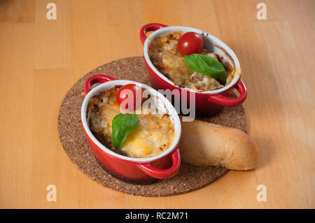 Homemade julien with mushrooms in two red, hot bowls. Chicken with mushrooms baked with cheese and a slice of bread on the wooden table Stock Photo
