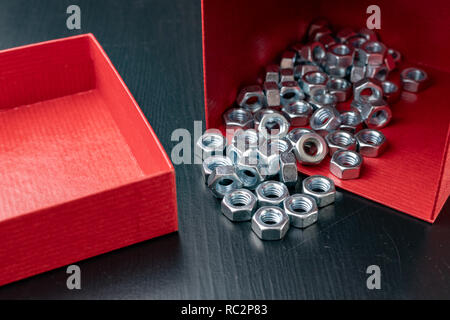 New nickel-plated screws in a red container. Accessories for mechanics on a wooden table. Dark background. Stock Photo