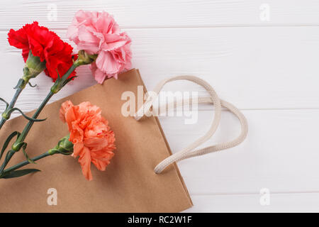 Colorful carnation flowers and shopping bag. White wooden surface background. Stock Photo