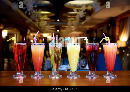 Row of different cocktails with straws on a blurred background. Stock Photo