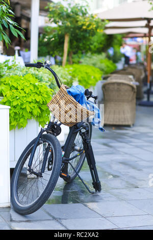 Bicycle with a basket stopped on the street next to the cafe. In the basket is a denim jacket, and next is a tripod for the camera. Stock Photo