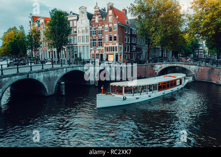 Beautiful view of Amsterdam canals with white cruise boat bridge and typical dutch houses. Holland Stock Photo
