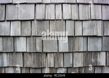 Wood shingle wall siding made of larch. Old, discolored and worn by weather shingles. Traditional austrian house siding. Stock Photo