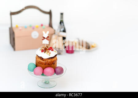 Easter cake, colored eggs and bottle of red wine. Easter composition with orthodox sweet bread, kulich and bottle of wine on light background. Gifts for holiday in wooden basket. Copyspace for text Stock Photo
