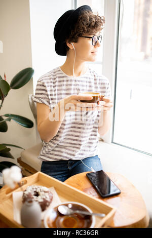 Pensive lady in hat drinking fresh-brewed coffee Stock Photo
