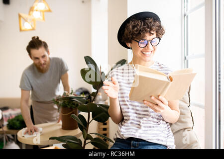 Excited lady in earphones reading book in cafe Stock Photo