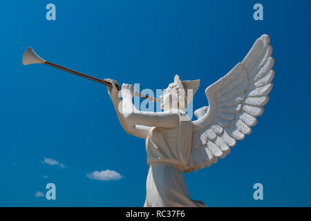 White sculpture of an angel holding  trumpet with the blue sky in the background, outdoors, sunny day. Stock Photo