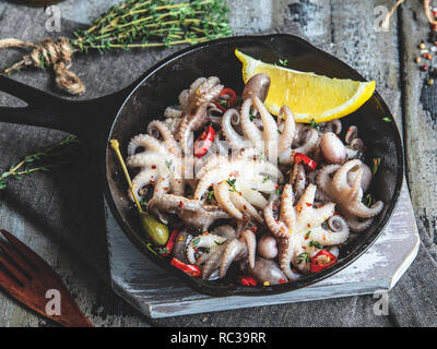 Baby octopus cooked, roasted in the iron pan portion, with lemon and seasoning Stock Photo