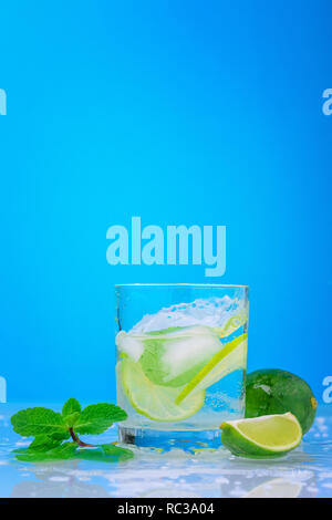 Splashing mojito cocktail with lime and fresh mint in glass on blue background Stock Photo