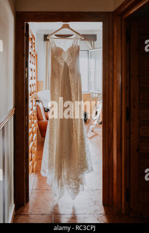 a white wedding dress hanging on a wooden door in a rustic house Stock Photo