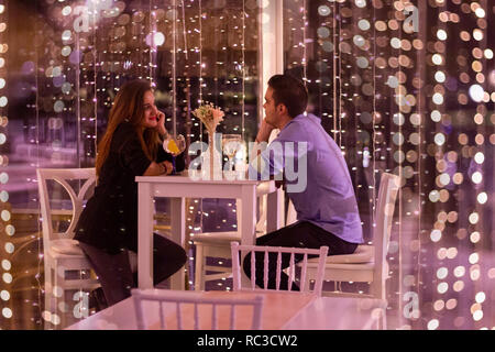 couple having a romantic dinner in a restaurant surrounded by lights Stock Photo