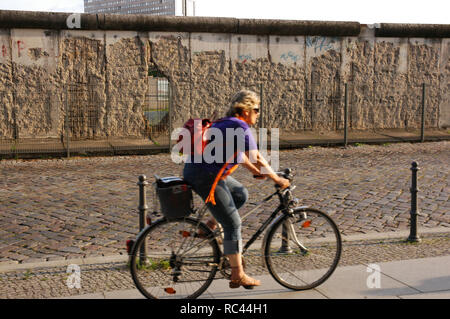 Woman cycling along the Berlin Wall in Niederkirchner Street. Berlin. Germany. Stock Photo