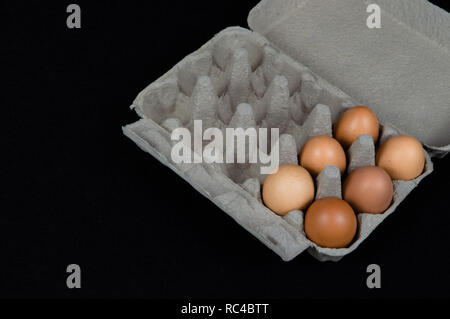 Six chicken eggs in a carton box, isolated on black felt background. Stock Photo