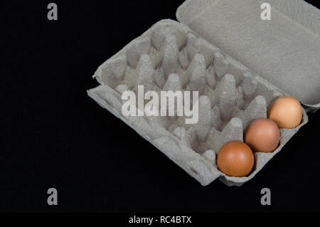 Three chicken eggs in a carton box, isolated on black felt background. Stock Photo