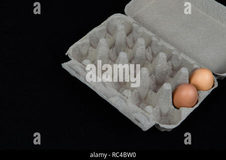 Two chicken eggs in a carton box, isolated on black felt background. Stock Photo