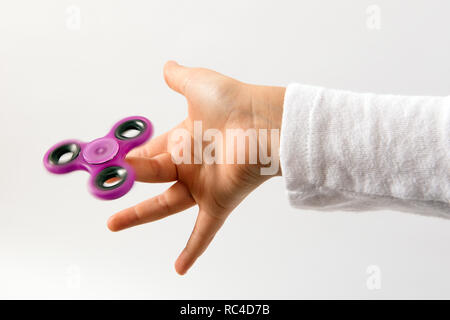 Purple spinner toy spinning on kids finger. Hand viewed in close up on white background Stock Photo