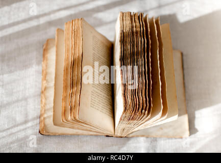 Open old book with spread faded pages, viewed in close-up from above on table with rustic white tablecloth Stock Photo