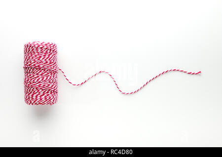 Reel with red and white string, curvy thread unrolled on white background, viewed from above Stock Photo
