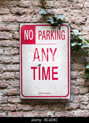 No Parking Any Time sign. Vintage white plate with red print, attached to old brick wall with ivy plant. Viewed in close-up and full frame Stock Photo