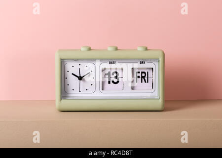 Small green vintage clock with white face and calendar showing Friday 13th. Viewed from the front in close-up, against pale pink background Stock Photo