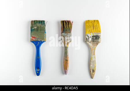 Three used paint brushes arranged in a row on white background with shadow, viewed in close-up from above Stock Photo