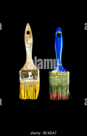 Two used paint brushes with withered remains of yellow, green and red paint, isolated on black background, viewed in close-up Stock Photo