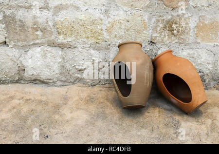 Two traditional big clay jars to storage water abandoned in the street. Pld stone wall background. Stock Photo